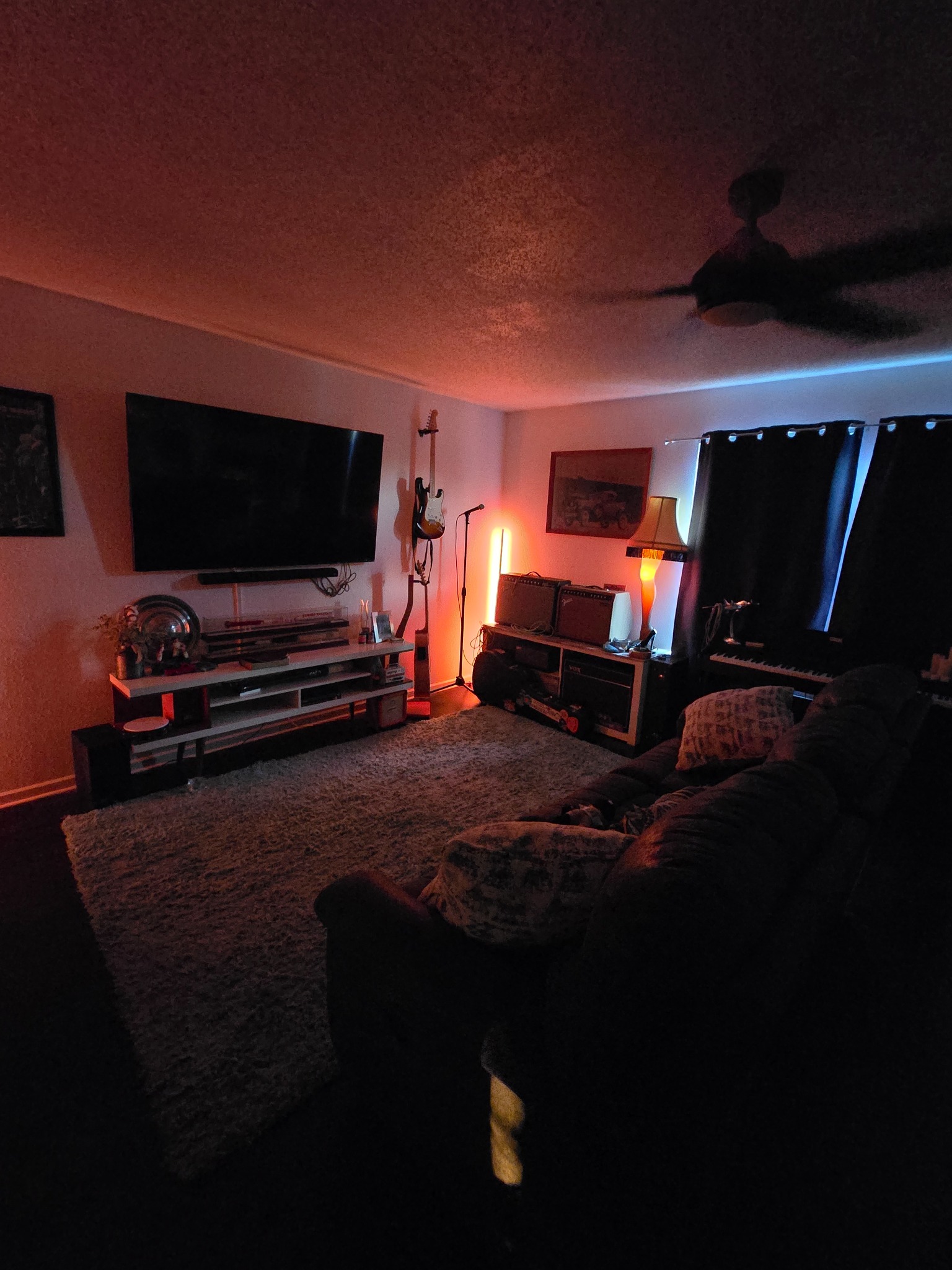 A home recording studio with guitars, amps, keyboard, microphone stand, and red-blue mood lighting.